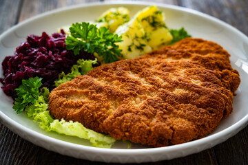 Crispy breaded fried pork chop, boiled potatoes and red cabbage served on white plate on wooden table
