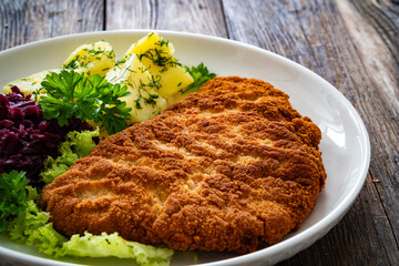Crispy breaded fried pork chop, boiled potatoes and red cabbage served on white plate on wooden table
