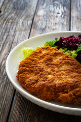 Crispy breaded fried pork chop, boiled potatoes and red cabbage served on white plate on wooden table
