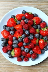 Different fresh ripe berries in bowl on wooden table, top view