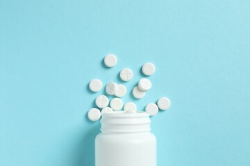 White pills pouring out of a medicine bottle on color background