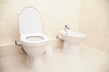 White Bidet and Toilet screwed in Bathroom,in Restroom, close-up. Beige Ceramic Floor Tiles. White...