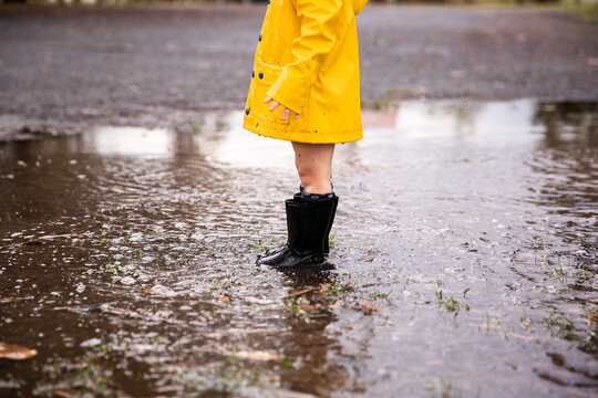 young person in gumboots and jacket in a puddle