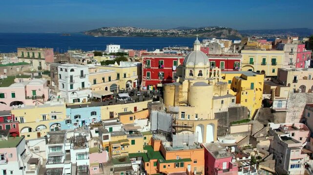 Procida Italy 4k aerial drone view of Corricella port and yellow church. Cinematic reveal of colorful houses and Terra Murata castle in Gulf of Naples. Authentic Mediterranean island scenery