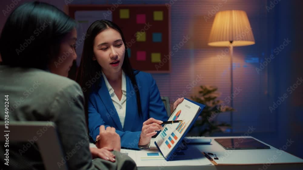 Poster two asian businesswomen are discussing and analyzing a business project together, with one of them p
