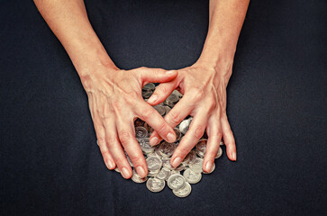 Hands cover heaps of silver coins. Close up concept of theft, misappropriation, fraud and greed.
