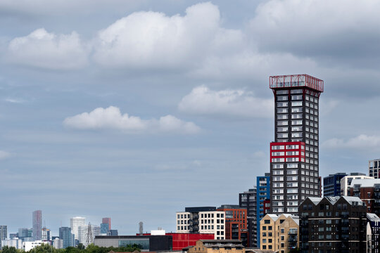 The image captures a modern skyscraper with distinctive red accents set against an expansive urban skyline under a cloudy sky, showcasing contemporary architecture  in London UK