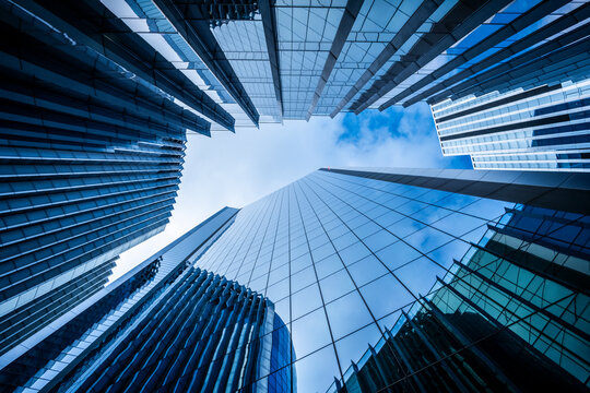 This image features skyscrapers in varying designs, all reaching up towards a blue sky, characterized by abstract blue tones and reflective surfaces, amidst urban landscapes  in London UK
