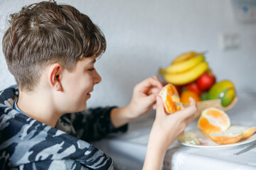 Young handsome teenager boy eating tasty ripe orange