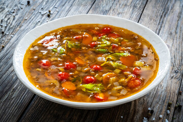 Fresh vegetable soup with chickpeas and lentil served in white bowl on wooden table
