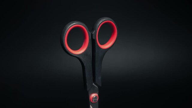 Scissors with red handles on a black background rotate close-up