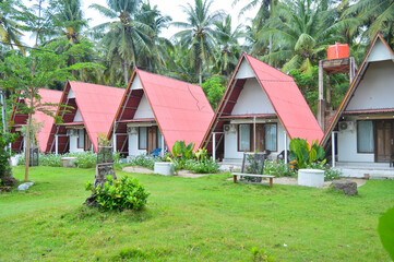 A row of charming A frame cottages with red roofs nestled among lush greenery and palm trees, creating a serene and picturesque tropical retreat