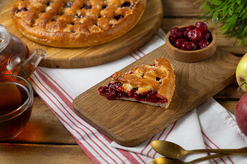Cherry pie with fresh berries. Cake shovel with piece of pie on rustic wooden background. Sweet summer dessert, halves of ripe cherry.