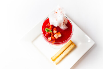 Red gelatin dessert in glass with whipped cream, cotton candy and strawberries in glass standind on white plate with two bread sticks isolated on white background