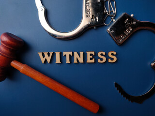 Top view wooden gavel and metal handcuff with text WITNESS on a blue background