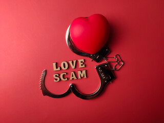 Top view metal handcuff and red heart shaped with text LOVE SCAM on a red background