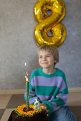 cute dreamy birthday boy looks at the cake and burning candles, number 8. birthday party. Holiday, congratulations, happiness, joy, pleasure