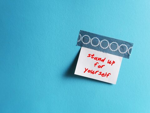 Stick note on blue copy space background written Stand up for yourself - assertiveness concept - ability to express your opinions and needs in a calm and open way - having boundaries and be assertive