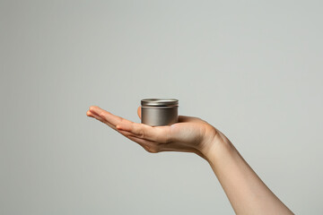 A hand holding a small silver jar white background, photography clear minimalism