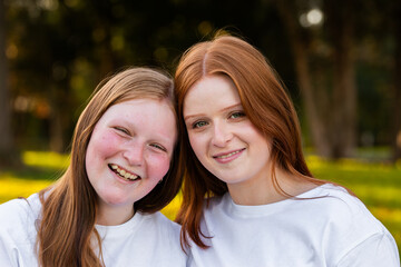 Portrait of twin seventeen year old redhead girls with heads together outdoors