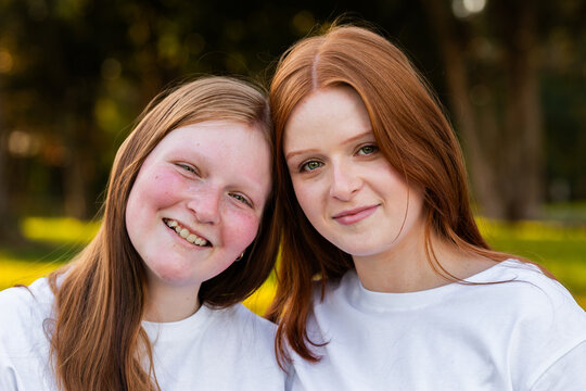 Portrait of twin seventeen year old redhead girls with heads together outdoors
