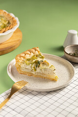Slice of savory vegetarian leek pie or quiche on white plate on light green background.