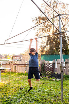 First Nations Australian boy swinging on hills hoist rotary clothesline in Aussie backyard