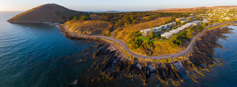 Aerial panorama of a winding coastal road around a rocky headland and housing community