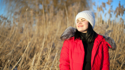 photo woman in the winter forest. girl in a snowy park. in a red jacket on the banks of a frozen river. winter walk in nature. Cold season. Beautiful girl smiling, sunny day.