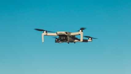 Small grey drone flying centred in front of cloudless blue sky