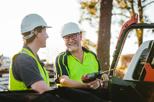 Two builders standing next to ute smiling, one holding a drill
