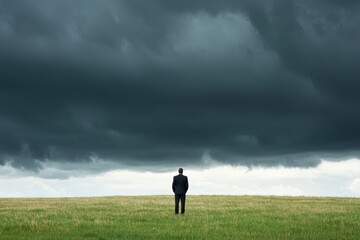 Fototapeta premium Business Professional Stands Alone in a Vast Open Field Under a Dramatic Cloudy Sky