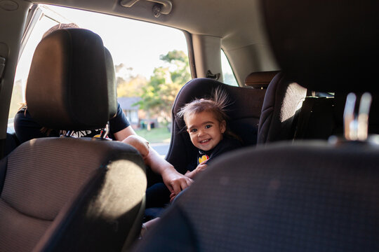 Australian mum putting Aboriginal toddler girl into forward facing car seat ready to travel