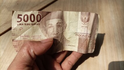 Hand holding Indonesian money, 5000 banknotes on a wood background