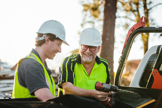 Two builders standing next to ute on construction site one man holding a drill