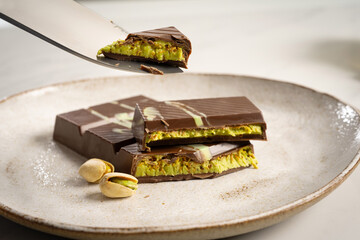 A broken bar of Dubai chocolate lies appetizingly on a ceramic plate and the delicious pistachio cream between the chocolate is clearly visible.