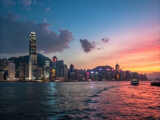 Obraz premium Stunning 4K Timelapse of Victoria Harbor Transitioning from Day to Night in Hong Kong, Capturing the Vibrant City Lights and Serene Waters Reflected in the Twilight Sky