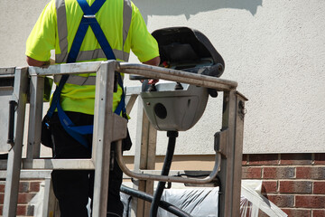 Worker on lifting platform using equipment to perform maintenance on building exterior during...