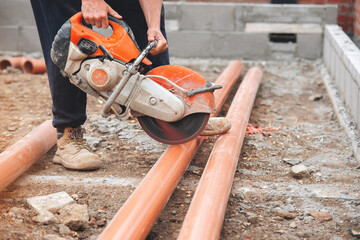 A construction worker uses a circular petrol saw to cut plastic drainage pipes at a building site 