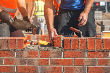 Bricklayers laying bricks and building a wall at a construction site on a sunny day
