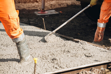 Concreters pouring and leveling fresh concrete for construction at a building site during daylight...