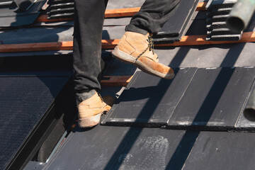 Roofer installing roof tiles around solar panels on a sloped roof during sunny weather in a residential area