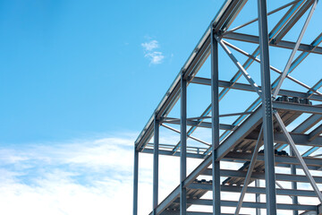 Steel frame construction under bright blue sky with scattered clouds during the day