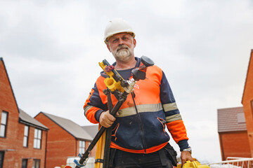 Buiilder with surveying equipment stands outside residential buildings on a cloudy day