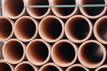 Stacked terracotta pipes arranged neatly on a construction site in sunny weather during the day