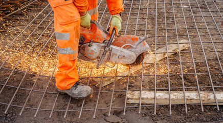 Construction worker cutting rebar on a job site while sparks fly under bright orange safety gear