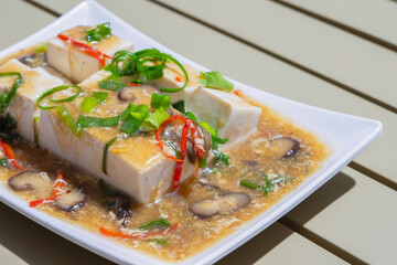 Stir-fried tofu or RAD na  tofu  with Chicken eggs, slide  spring onions, mushrooms and red chili peppers. Healthy vegetarian food on a white plate.