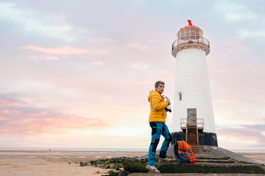 A photographer captures the beauty of a lighthouse at sunset by the beach, enjoying a tranquil moment in nature - Powered by Adobe