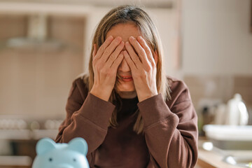 Frustration woman sits at the kitchen table, covering her face with her hands