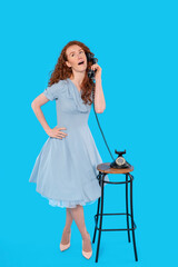 Young woman in a light blue dress talking on a vintage phone against a bright blue background in a playful pose